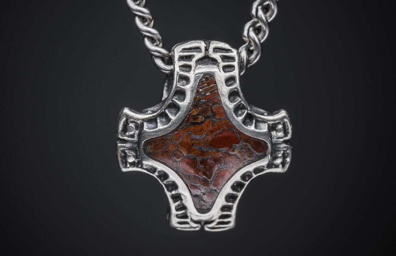 Silver Mjölnir pendant with an oxidized finish and reddish-brown inlay featuring an intricate web-like pattern, on a twisted chain.