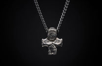 Silver metal pendant necklace featuring an intricate, stylized hammer design with a central circular emblem, on a dark background.
