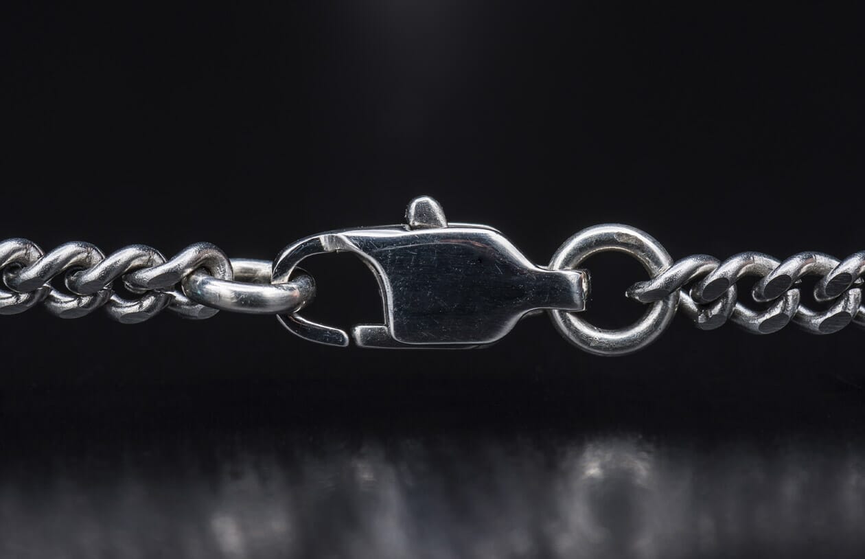 Close-up of a silver metal curb chain necklace featuring a prominent lobster clasp.