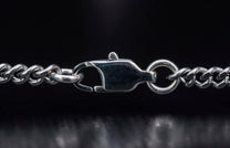Close-up of a silver metal curb chain necklace featuring a prominent lobster clasp.