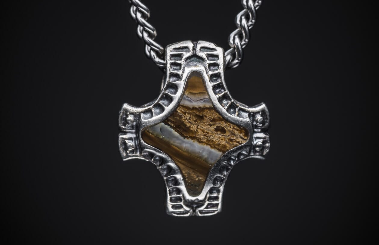 Textured silver-toned pendant featuring a brown and white banded stone inlay, suspended from a braided chain.