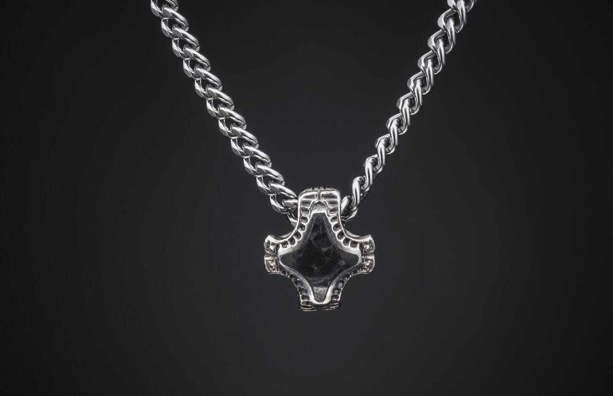 Silver braided chain necklace with a dark, intricately designed Mjolnir-style pendant on a dark background.