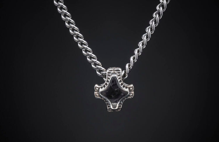Silver braided chain necklace with a dark, intricately designed Mjolnir-style pendant on a dark background.