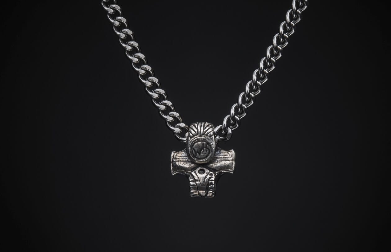 Silver metal necklace with a textured hammer-shaped pendant featuring a stylized face, centered on a black background.