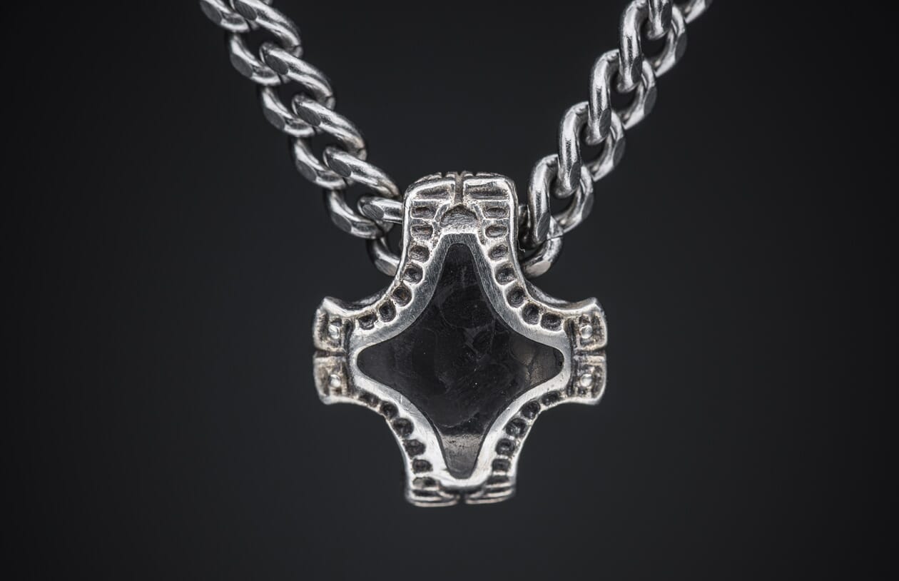 Silver-toned metal pendant with a dark diamond-shaped insert and textured, dotted arms, on a matching chain, close-up.