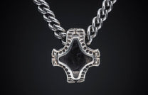 Silver-toned metal pendant with a dark diamond-shaped insert and textured, dotted arms, on a matching chain, close-up.