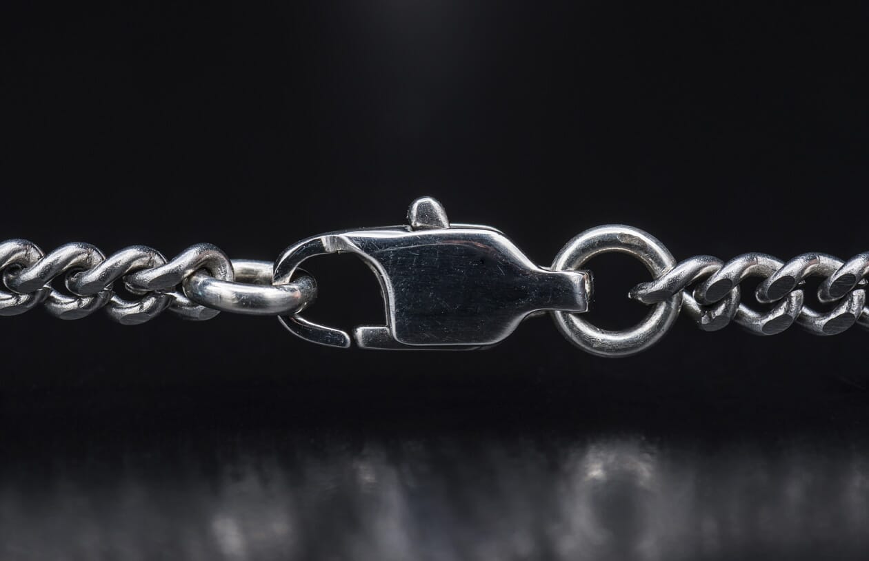 Silver chain featuring interlocking curb links and a polished lobster claw clasp against a dark background.