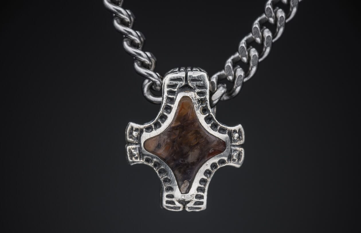 Ornate silver pendant featuring a reddish-brown patterned stone, suspended from a silver curb chain.
