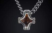 Ornate silver pendant featuring a reddish-brown patterned stone, suspended from a silver curb chain.