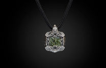 Silver-toned metal pendant with a dark green textured stone, featuring intricate designs, on a black braided cord.