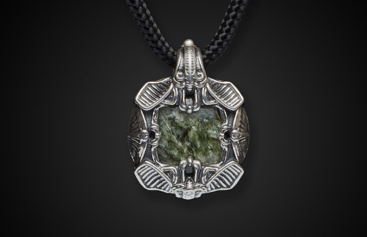 Silver pendant with an intricate alien-insectoid design, centering a rectangular marbled green stone, on a braided black cord.