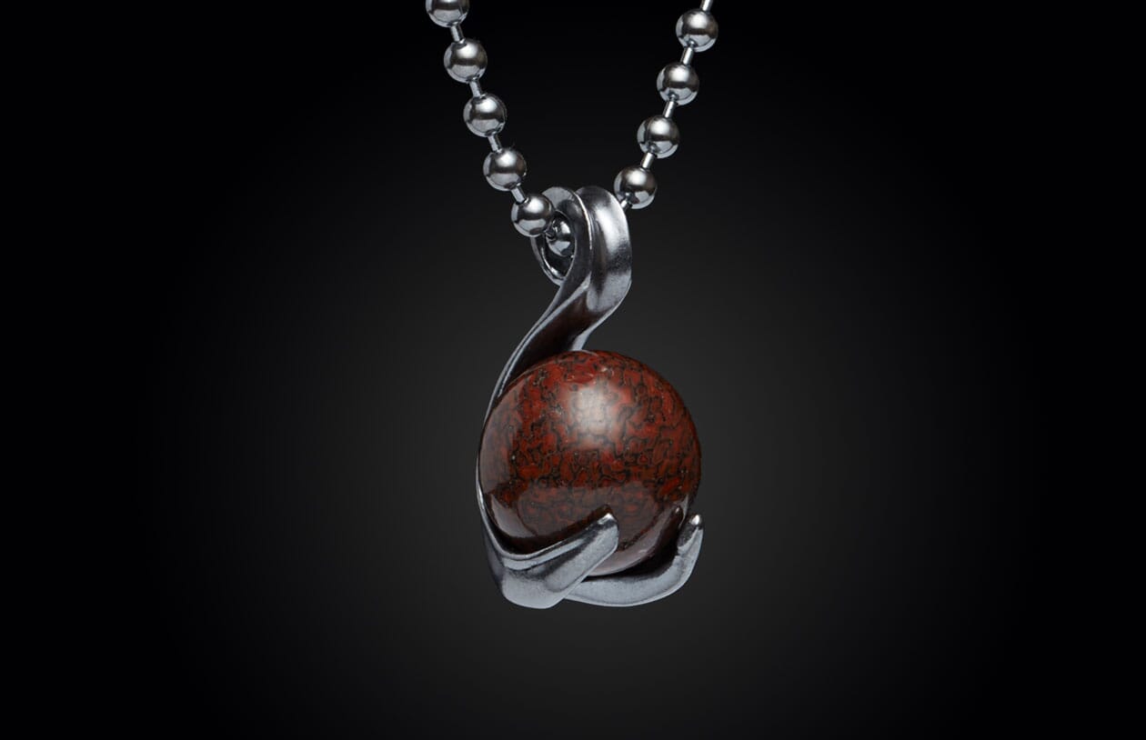 Silver-toned metal necklace pendant holding a spherical dark red stone with black speckled patterns, on a beaded chain.