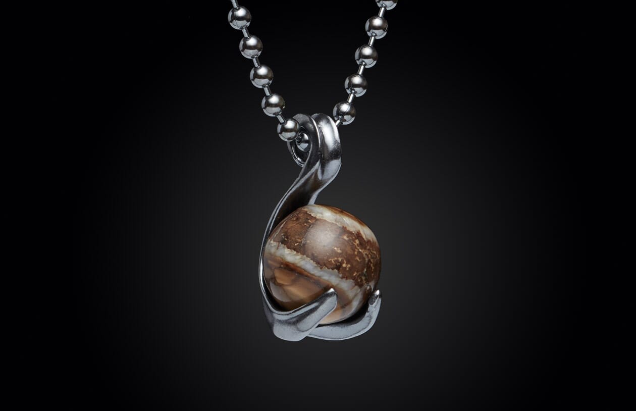 Round brown and white stone pendant in a silver-tone setting on a ball chain, against a black background.
