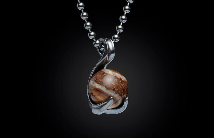 Round brown and white stone pendant in a silver-tone setting on a ball chain, against a black background.