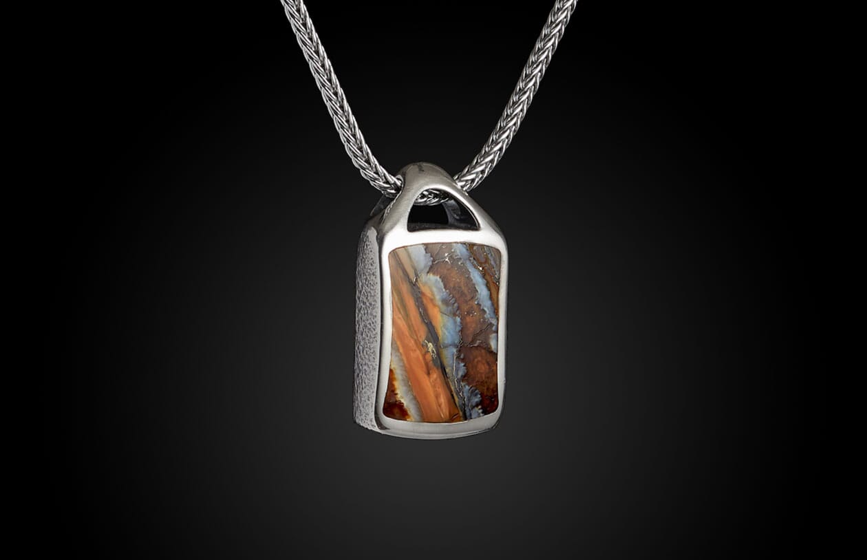 Silver pendant necklace with a multi-colored, layered orange, blue, and brown stone in a textured setting on a braided chain.