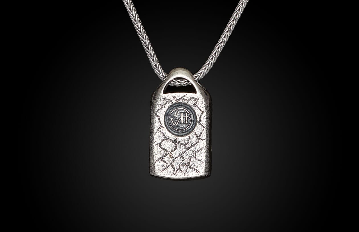Silver necklace with a textured rectangular pendant featuring a circular "WH" emblem, on a braided chain.