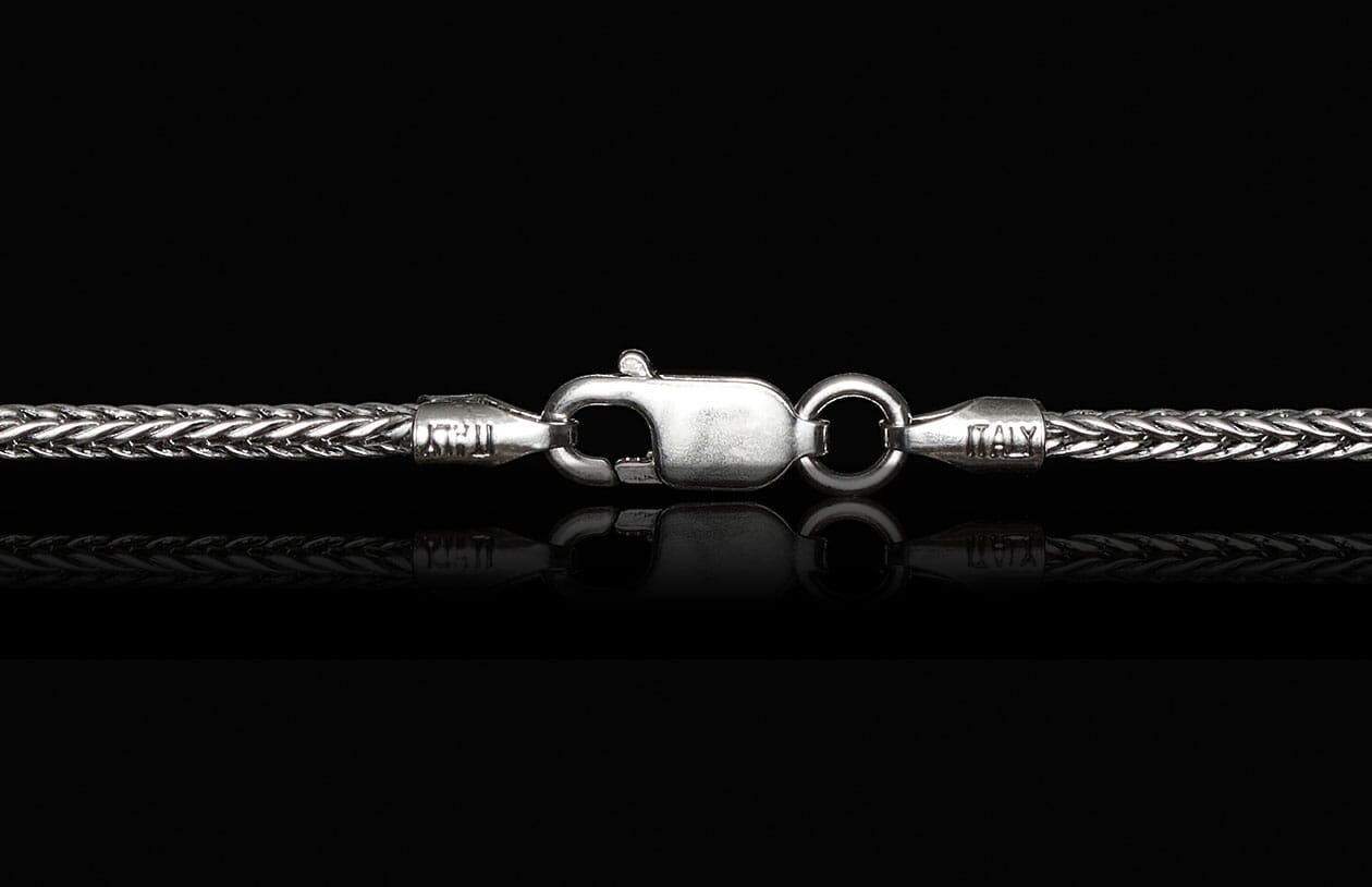 Silver braided chain with a lobster clasp, engraved "ITALY", on a reflective black surface.
