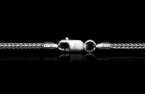 Silver braided chain with a lobster clasp, engraved "ITALY", on a reflective black surface.