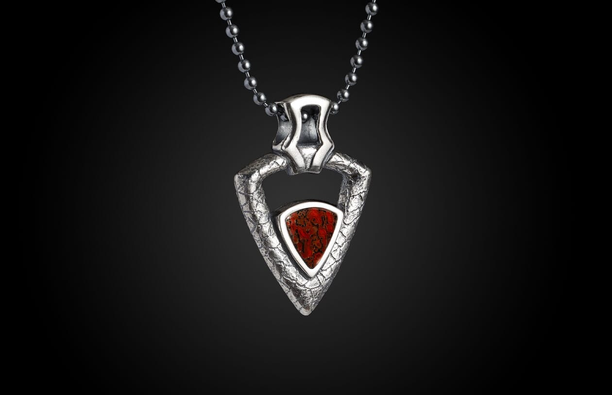 Triangular silver pendant with a textured finish and a red fossilized inlay, hanging from a metal bead chain.
