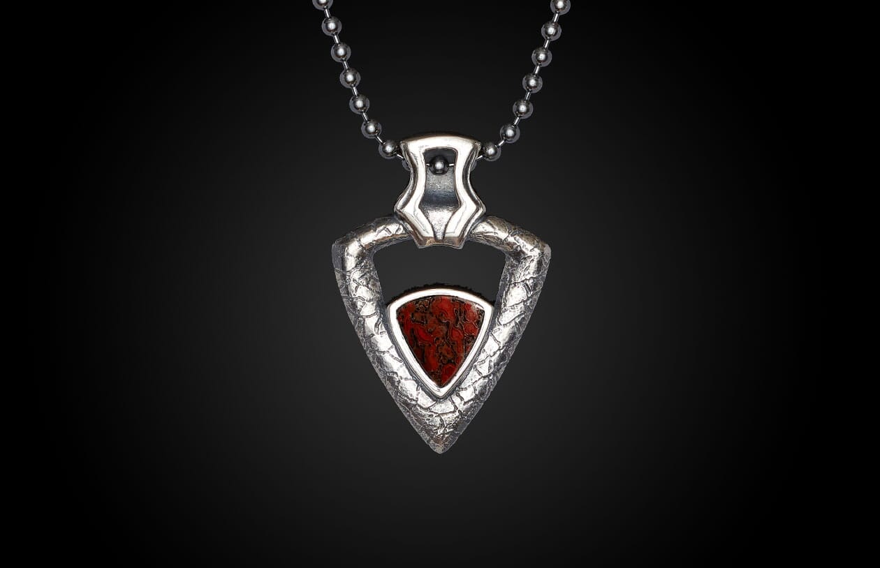 Silver necklace with a triangular red stone pendant, featuring a textured silver frame, displayed against a dark background.