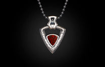 Silver necklace with a triangular red stone pendant, featuring a textured silver frame, displayed against a dark background.