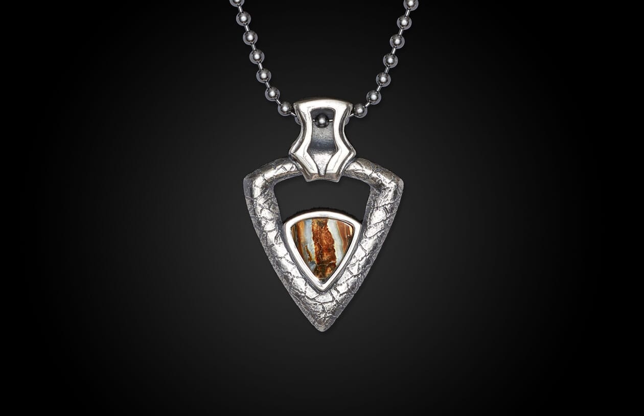 Silver-toned arrowhead pendant with a textured metal frame and a striped brown, orange, and white stone, hanging on a ball chain.