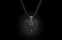 A dark grey pendant by William Henry, shield-shaped, with a silver rivet and etched logo, on a black braided cord.
