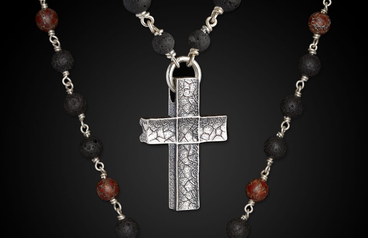 Silver textured cross pendant on a necklace of black lava beads and red marbled accent beads.