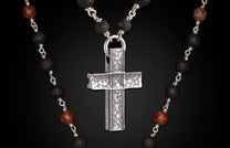 Silver textured cross pendant on a necklace of black lava beads and red marbled accent beads.
