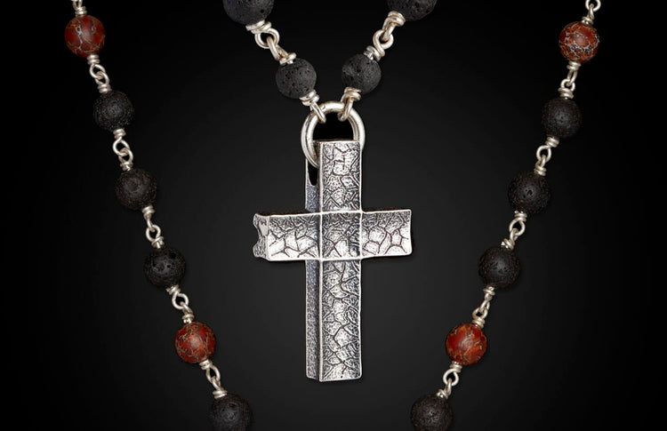 Silver textured cross pendant on a necklace of black lava beads and red marbled accent beads.