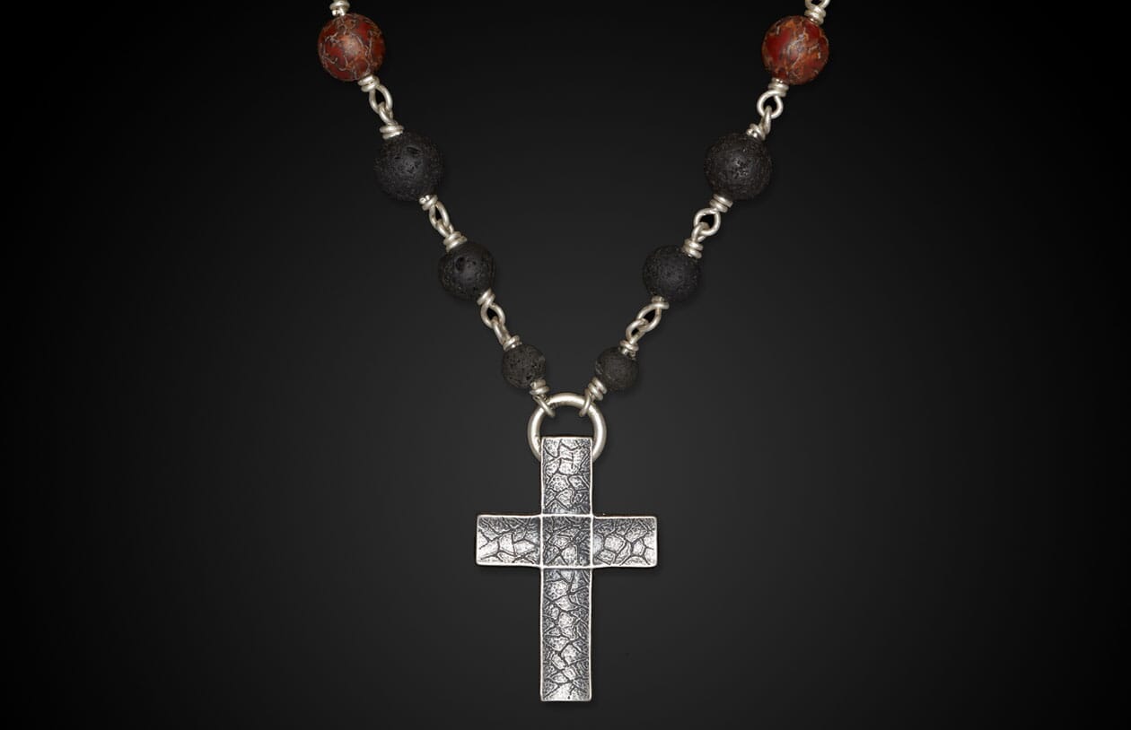 Silver-toned textured cross necklace with black lava beads and reddish-brown patterned beads.