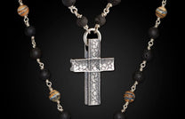 Textured silver cross pendant on a beaded necklace with porous black lava and striped natural stone beads.