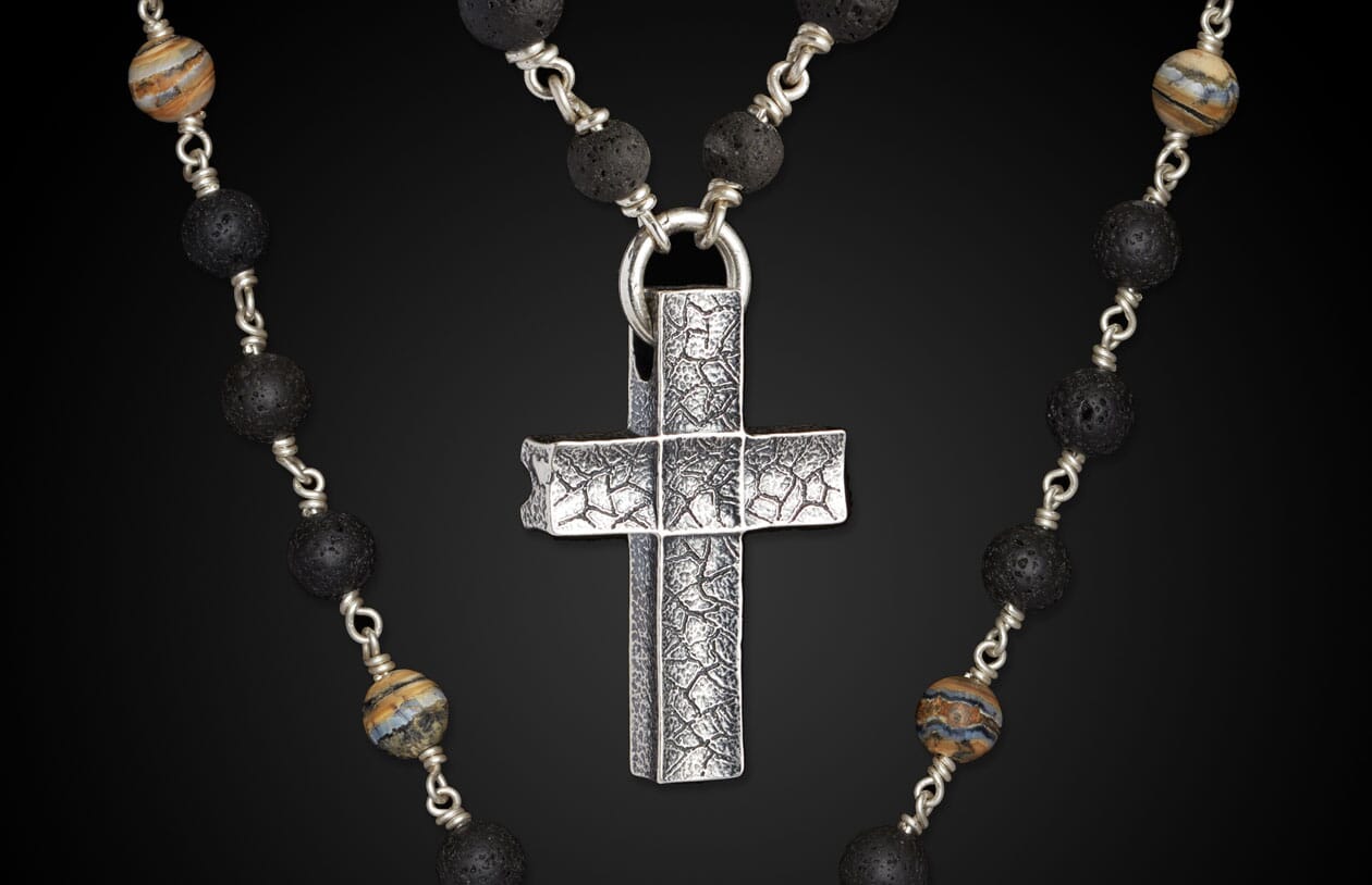 Textured silver cross pendant on a beaded necklace with porous black lava and striped natural stone beads.