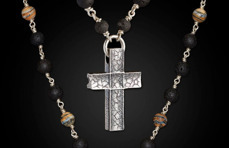 Textured silver cross pendant on a beaded necklace with porous black lava and striped natural stone beads.