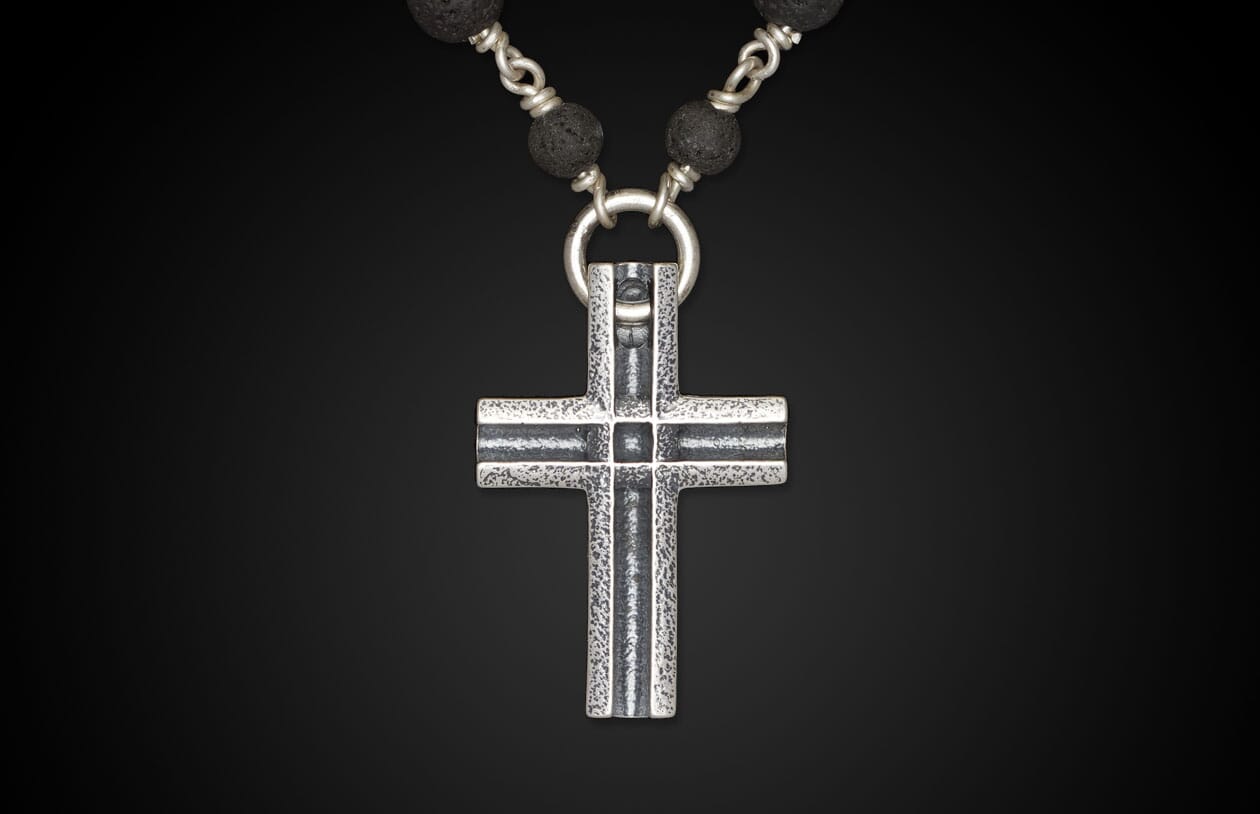 Silver cross pendant with a rugged texture, hanging from a necklace of dark, textured lava beads.