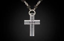 Silver cross pendant with a rugged texture, hanging from a necklace of dark, textured lava beads.