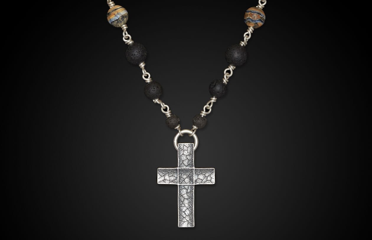 Textured silver cross pendant necklace with black lava beads and striped accent beads.