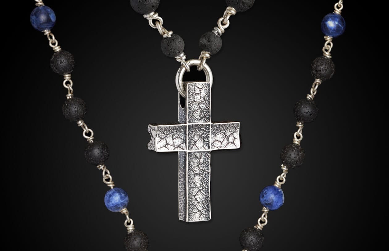 Sodalite and lava stone beaded necklace with a silver cross pendant featuring a distressed, grid-like texture.