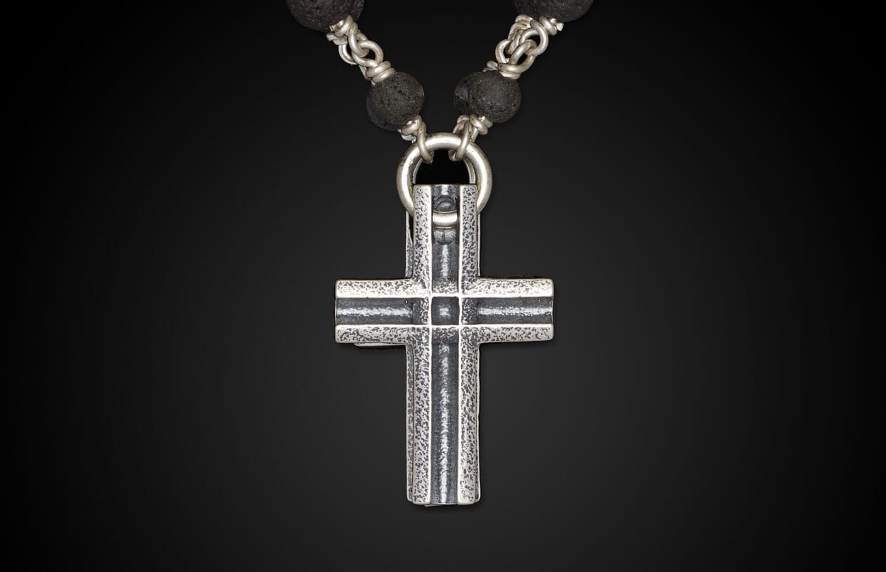 Textured silver cross pendant hanging from a necklace of black lava stone beads and intertwined silver links.