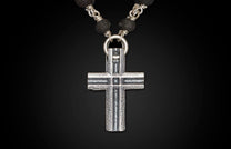 Textured silver cross pendant hanging from a necklace of black lava stone beads and intertwined silver links.