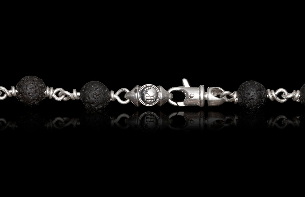 Sodalite Crux beaded chain with black porous lava stone beads, silver links, a central engraved charm, and a lobster clasp.