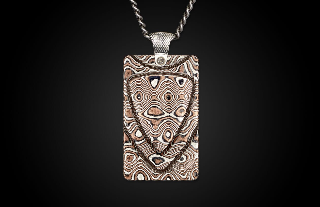 Rectangular mokume-gane pendant by Mokume Forge with a silver chain, featuring a swirling copper and silver wood-grain pattern and textured bail.
