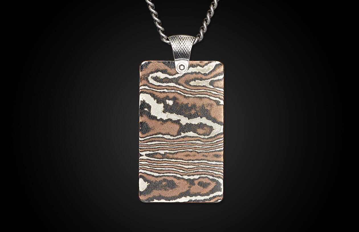Rectangular metal pendant with a silver chain and bail, featuring a swirling woodgrain pattern in copper, silver, and dark tones.
