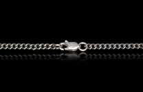 Silver curb chain by Mokume Forge with a lobster clasp featuring a circular emblem, reflected on black.