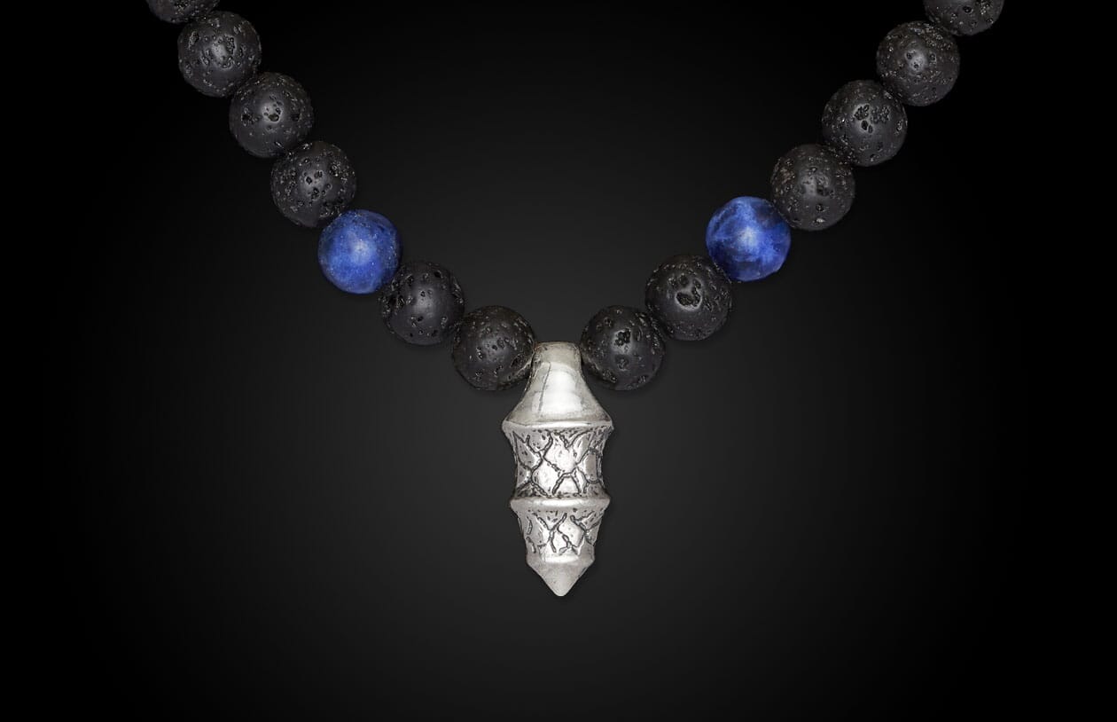 Black lava bead necklace with vibrant blue sodalite beads and a detailed silver geometric pendant, hanging centrally.