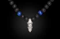 Black lava bead necklace with vibrant blue sodalite beads and a detailed silver geometric pendant, hanging centrally.