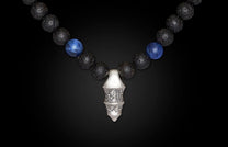 Sodalite necklace with blue sodalite and black lava beads, featuring a textured silver-toned pendant with carved details.