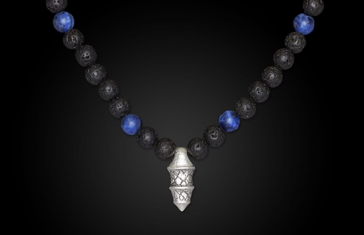 Black lava and blue sodalite beaded necklace with an ornate silver pendant on a dark background.