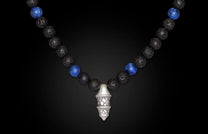 Black lava and blue sodalite beaded necklace with an ornate silver pendant on a dark background.