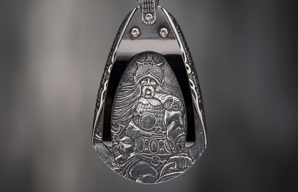 Silver-toned metal pendant featuring an intricately engraved warrior in a helmet, holding a sword.